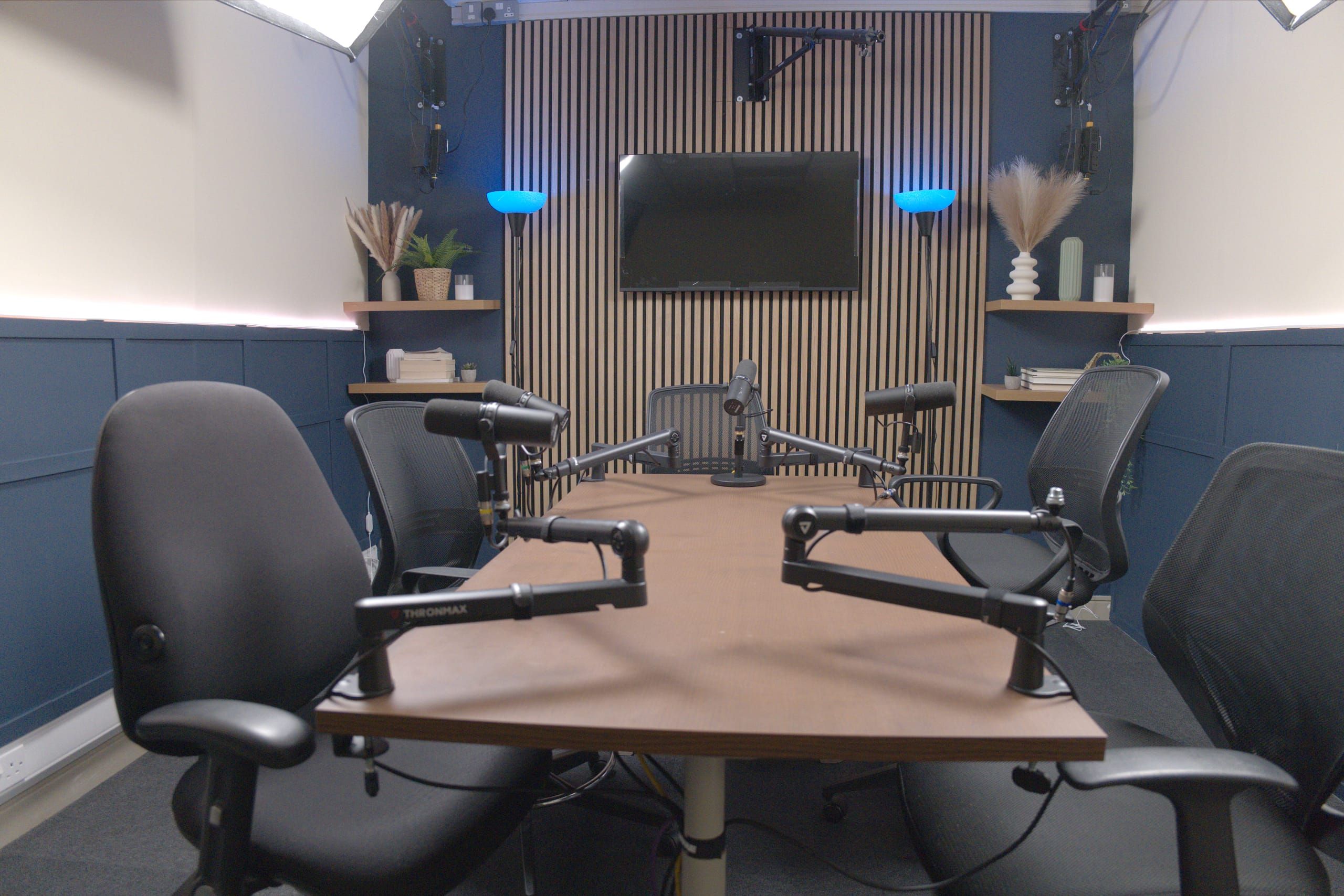 Room 4 at Myriad Studios: black office chairs around a central table with boom microphones, in front of a navy wall and wooden slat backdrop