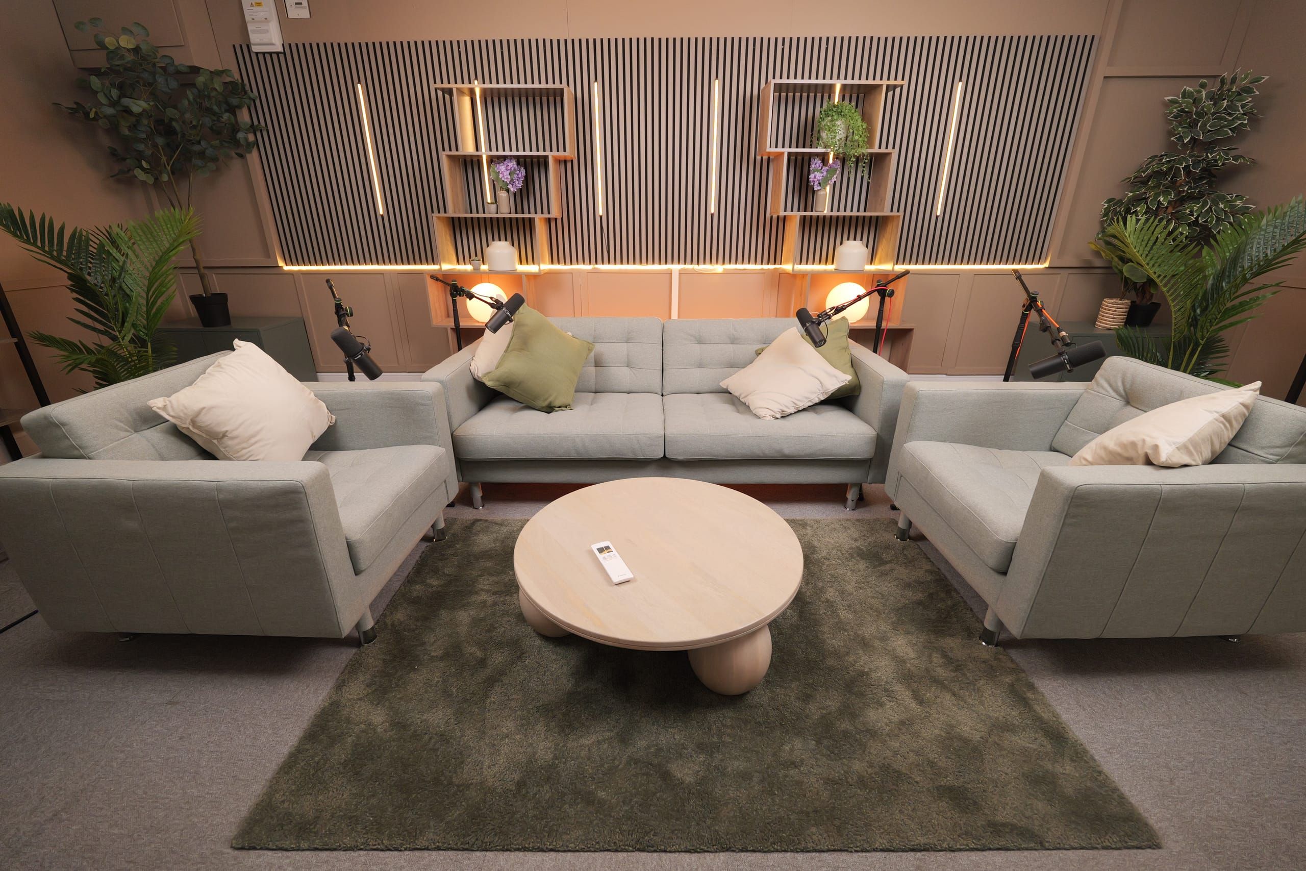 Room 2 at Myriad Studios: sage lounge seating in front of a lit slat wall with microphones on stands