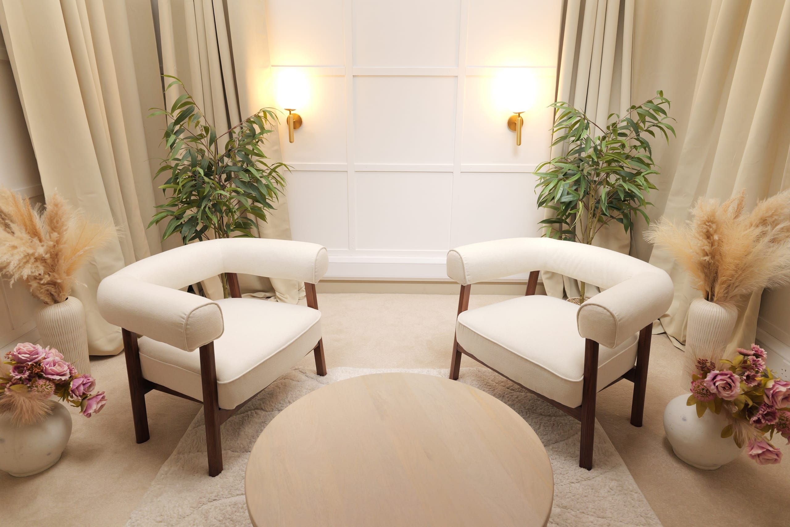 Room 3 at Myriad Studios: two cream armchairs either side of a round table, with brass wall lights and pampas grass